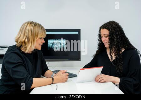 Femme souriante lisant un rapport médical devant une femme dentiste à la clinique Banque D'Images