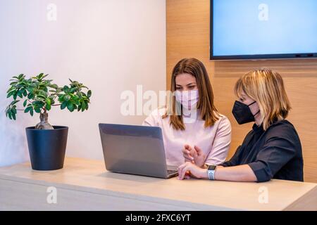 Femme dentiste et réceptionniste portant un masque facial de protection discutant sur un ordinateur portable au bureau de la clinique Banque D'Images