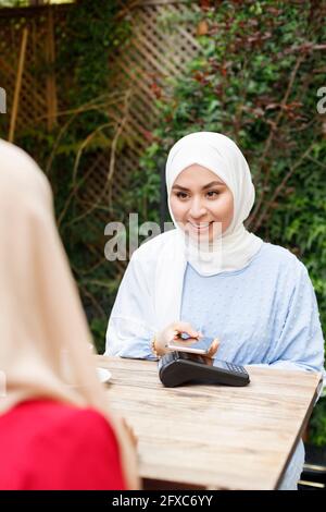Jeune femme utilisant un téléphone mobile tout en payant au café-terrasse Banque D'Images