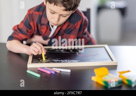 Un garçon qui dessine avec des craies colorées sur une ardoise à la maison Banque D'Images