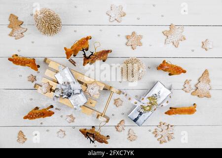 Cadeaux de Noël et traîneau à jouets entourés de cerfs-jouets avec biscuits faits maison sur fond de bois blanc Banque D'Images