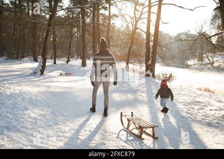 Père marchant avec son fils tout en tirant sur la neige pendant l'hiver Banque D'Images