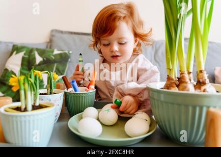 Jolie fille regardant les oeufs dans l'assiette par plante en pot pendant Pâques Banque D'Images