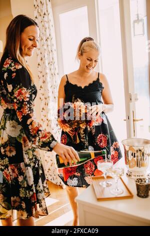 Femme souriante servant du champagne en verre tout en se tenant debout par un ami Banque D'Images