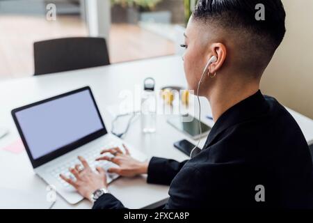 Jeune femme d'affaires avec écouteurs intra-auriculaires travaillant sur un ordinateur portable au bureau Banque D'Images