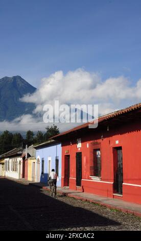 ANTIGUA, GUATEMALA - 01 août 2019 : maisons basses et colorées sur une rue pavée avec un homme sur un vélo, ciel bleu en arrière-plan et volcan d'eau Banque D'Images