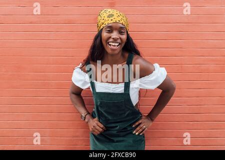 Femme gaie avec main sur la hanche par mur Banque D'Images
