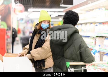 Des amies en vêtements chauds achetant des articles d'épicerie au supermarché pendant la COVID-19 Banque D'Images