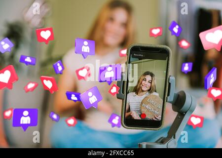 Une adolescente souriante sur l'écran d'un téléphone portable parmi les icônes des réseaux sociaux à la maison Banque D'Images