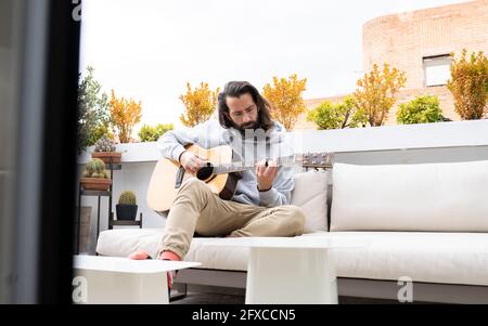 Homme avec de longs cheveux jouant de la guitare dans le balcon Banque D'Images