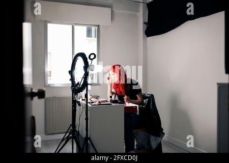 Maquilleuse aux cheveux teints appliquant un eyeliner tout en filmant au studio à l'aide d'un téléphone portable Banque D'Images