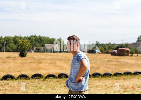 Recentrer un jeune homme caucasien sérieux dans une chemise à rayures debout dans le profil sur le terrain de jeu. Portrait caucasien. Campagne. Hors foyer Banque D'Images