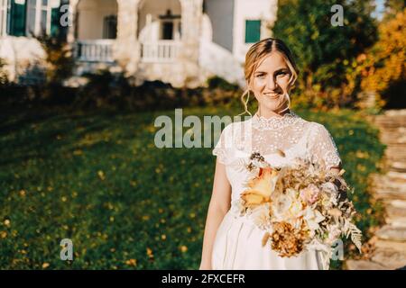 Mariée souriante tenant bouquet de fleurs pendant la cérémonie de mariage Banque D'Images