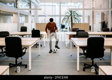 Jeune entrepreneur jouant avec le ballon de football au bureau Banque D'Images