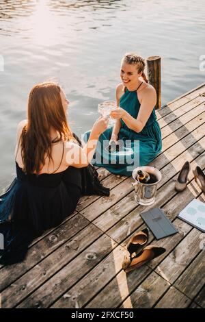 Des femmes souriantes planiguaient des événements pour toaster le champagne tout en étant assise sur la jetée au-dessus du lac Banque D'Images