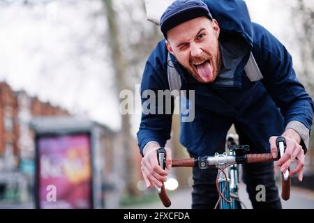 Jeune homme qui colle à la langue pendant qu'il roule à vélo Banque D'Images