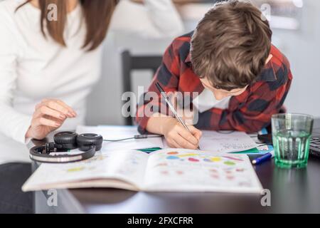 Garçon faisant des devoirs par la mère à la maison Banque D'Images