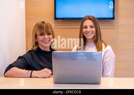 Femme dentiste et réceptionniste souriant assis devant un ordinateur portable à la réception Banque D'Images