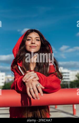 Femme adolescente souriante vêtue d'une veste rouge penchée sur un tuyau pendant la journée ensoleillée Banque D'Images