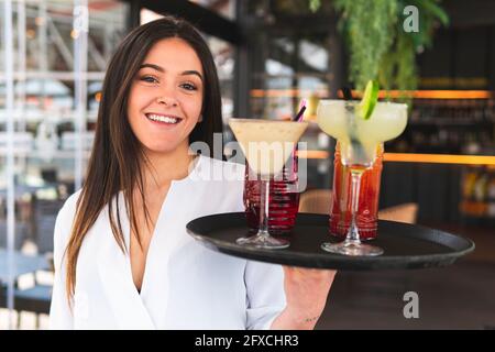 Un beau barman souriant qui tient un plateau de cocktails au bar Banque D'Images