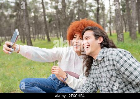 Une jeune femme heureuse avec un homme qui prend son selfie à travers un smartphone en forêt Banque D'Images