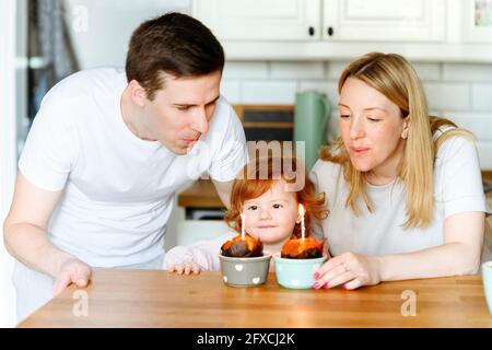 Fille regardant les bougies au milieu des parents dans la cuisine Banque D'Images