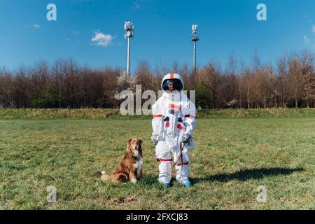 Astronaute féminin en costume spatial debout avec un chien sur l'herbe Banque D'Images