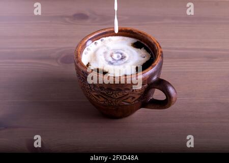 Café et lait dans une tasse en faïence. Le lait est versé dans le café Banque D'Images