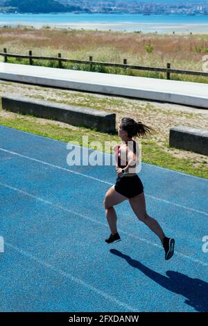 Vue arrière d'une jeune sprinteuse qui court sur un piste d'athlétisme Banque D'Images