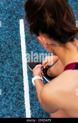 Crop Young sportswoman nouant des lacets sur la piste Banque D'Images