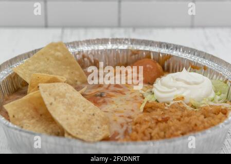 Grande boîte contenant une enchilada recouverte de fromage fondu, servie avec des haricots réfrits et du riz. Banque D'Images