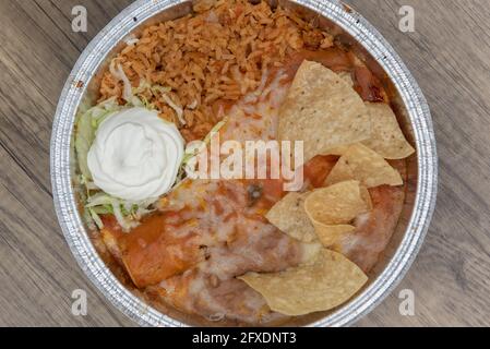 Vue en hauteur d'une grande boîte contenant une enchilada couverte de fromage fondu, servi avec des haricots réfrits et du riz. Banque D'Images