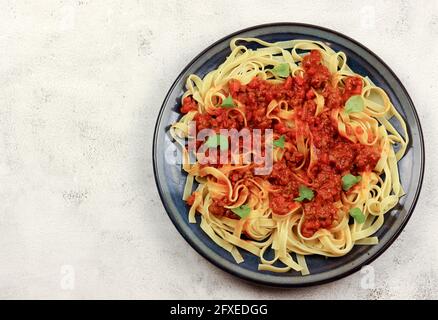 Un plat traditionnel italien classique, Tagliatelle alla Bolognese, des pâtes aux œufs plats avec une sauce à la viande sur une assiette ronde sur fond gris clair. Vue de dessus Banque D'Images