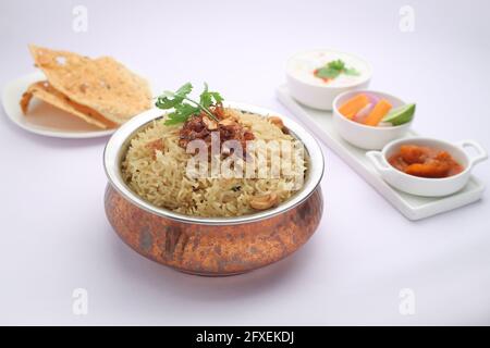 Veg Biriyani, garni d'oignon frit, de feuilles de coriandre et de noix de cajou frite dans un ancien récipient en laiton avec du pickle au citron, salade de légumes, rautha et apl Banque D'Images