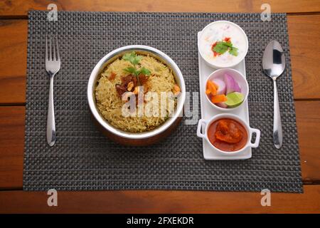 Veg Biriyani, garni d'oignon frit, de feuilles de coriandre et de noix de cajou frite dans un ancien récipient en laiton avec du pickle au citron, salade de légumes, rautha et un p Banque D'Images