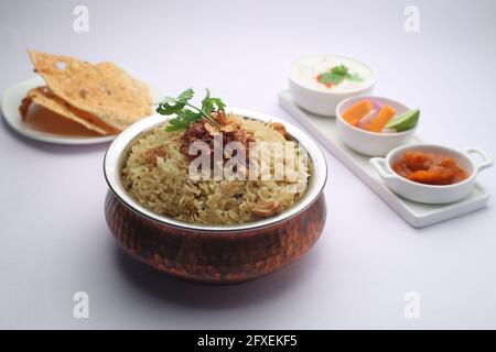 Veg Biriyani, garni d'oignon frit, de feuilles de coriandre et de noix de cajou frite dans un ancien récipient en laiton avec du pickle au citron, salade de légumes, rautha et un p Banque D'Images