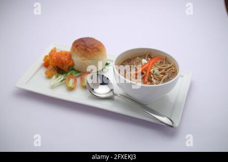 Soupe de manchow au poulet, garnie de légumes et de nouilles disposées dans un bol blanc avec texture ou arrière-plan blanc Banque D'Images