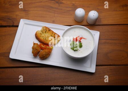 Soupe à la crème de champignons dans un bol blanc avec pain grillé et salade de légumes frais comme accompagnement disposés sur une table de service blanche avec du bois Banque D'Images