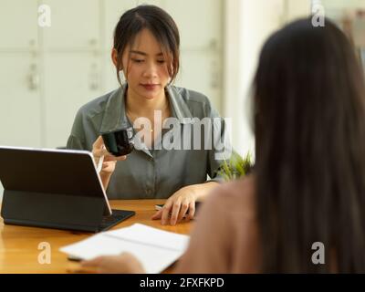 Portrait de deux employées de bureau consultant d'autres travaux pendant assis l'un en face de l'autre sur le lieu de travail Banque D'Images