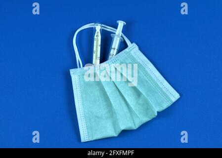 Seringue et thermomètre médicaux dans un masque facial sous forme de sac. Stratégie de vaccination et de traitement pendant la pandémie du coronavirus. Banque D'Images