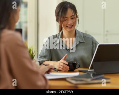 Prise de vue courte d'une employée de bureau amicale souriant et tenant en étant assis en face de son collègue dans la salle de bureau Banque D'Images