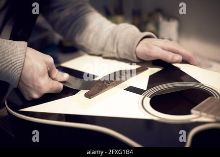 Un employé de service répare une guitare avec un outil, photo tonifiée. Banque D'Images