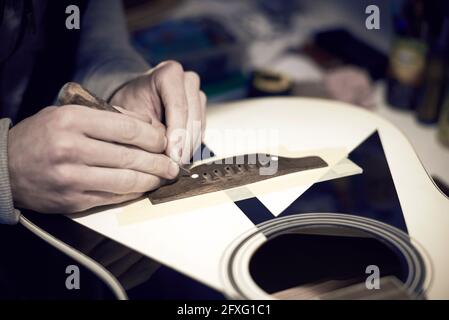 Un employé de service répare une guitare avec un outil, photo tonifiée. Banque D'Images