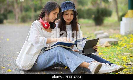 Vue latérale des étudiantes en plein air étudiant ensemble, lisant des livres tout en étant assis dans le parc à l'université Banque D'Images