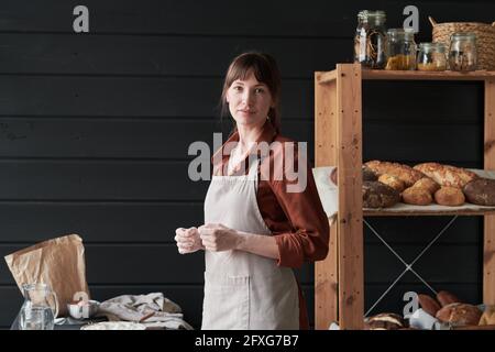 Portrait d'une jeune femme en tablier regardant la caméra pendant cuisson dans la cuisine Banque D'Images