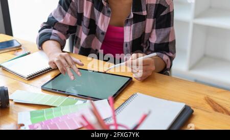 Photo rognée d'une étudiante de designer en cours de réalisation avec le numérique tablettes et fournitures de créateur dans la bibliothèque Banque D'Images