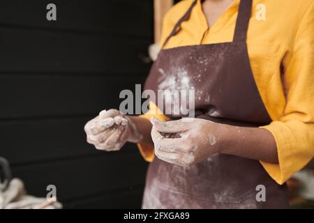 Gros plan de la jeune femme avec de la farine sur son tablier et sur ses mains cuisiner dans la cuisine Banque D'Images