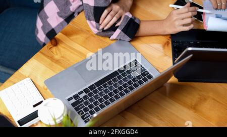 Vue de dessus d'un espace de travail confortable avec ordinateur portable, calculatrice et deux personnes consultant sur leur travail Banque D'Images