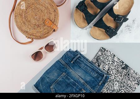 Flat lay avec vêtements et accessoires été pour femme. T-shirt à imprimé animal, sandales, short en denim bleu, sac en rotin biologique tendance, lunettes de soleil. V Banque D'Images