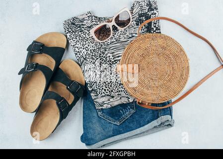 Flat lay avec vêtements et accessoires été pour femme. T-shirt à imprimé animal, short en denim bleu, sac en rotin biologique tendance, lunettes de soleil. Vacances, Banque D'Images